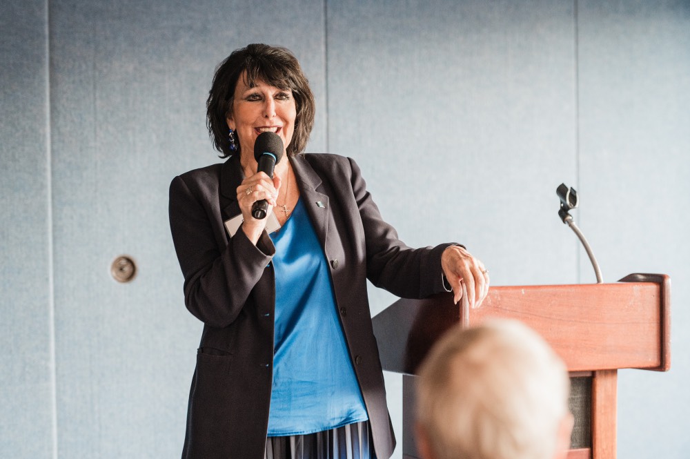 President Mantella smiling as she speaks to GVSU Alumni in D.C., arm rested on podium